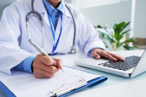 A doctor writing while operating laptop